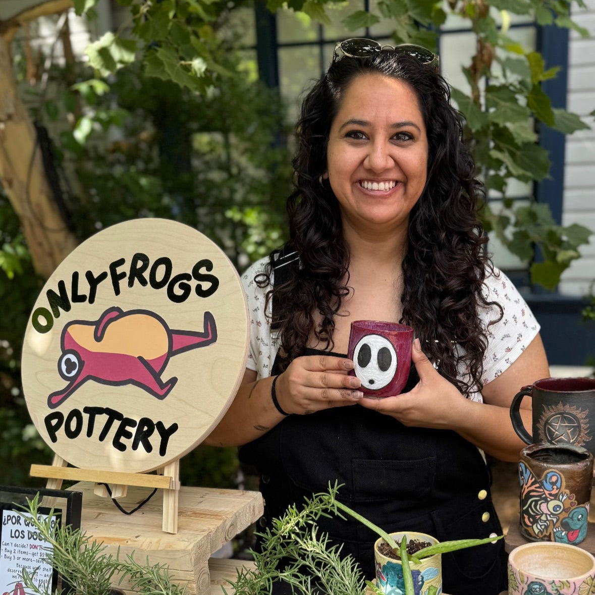 Woman holding a ceramic mug with 'Only Frogs Pottery' sign in the background