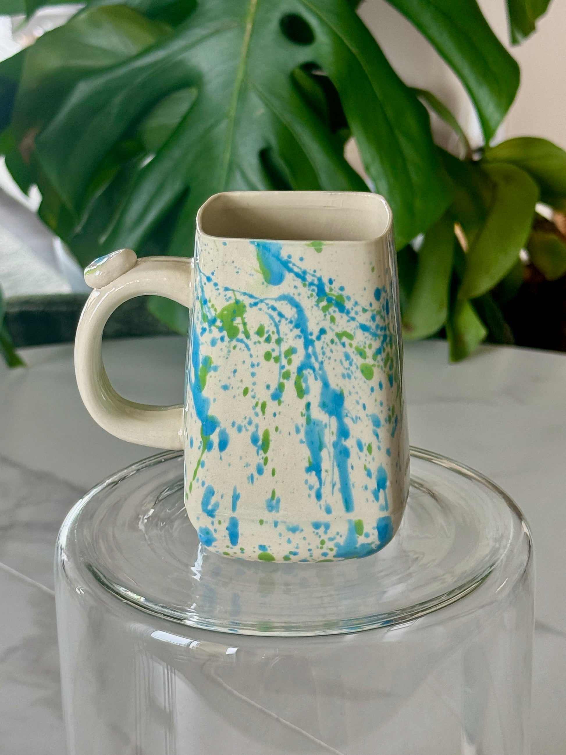 Splatter square mug front view showing blue and green splatter glaze on cream body