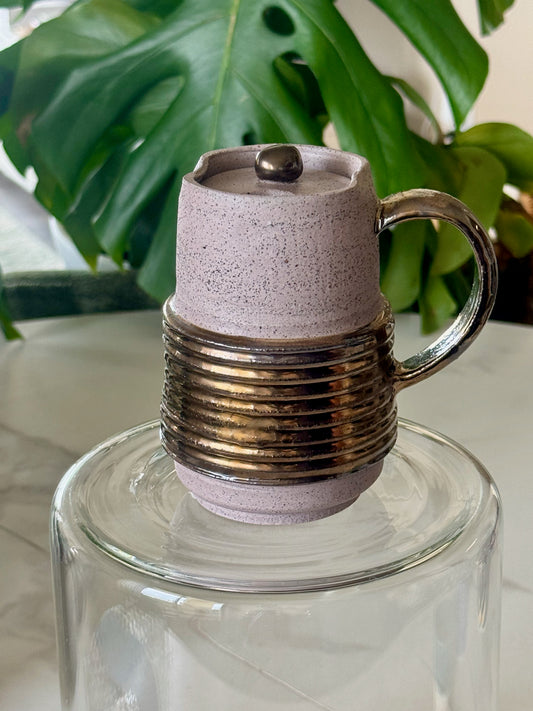 Locking travel mug front view showing coiled bronze band and speckled lavender glaze with lid