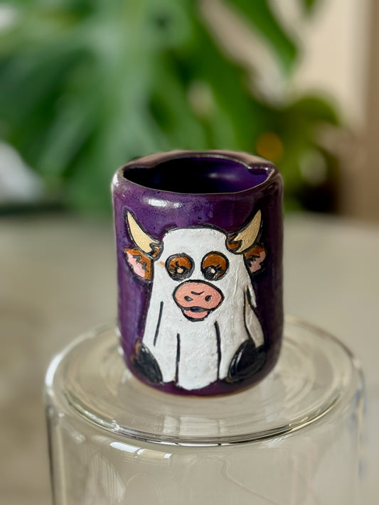 Ghost cow Halloween travel cup front view showing hand-illustrated white ghost cow on deep purple glaze
