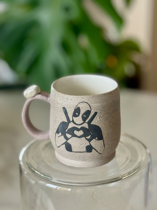 Deadpool heart mug front view showing sgraffito Deadpool making a heart on speckled sandy clay