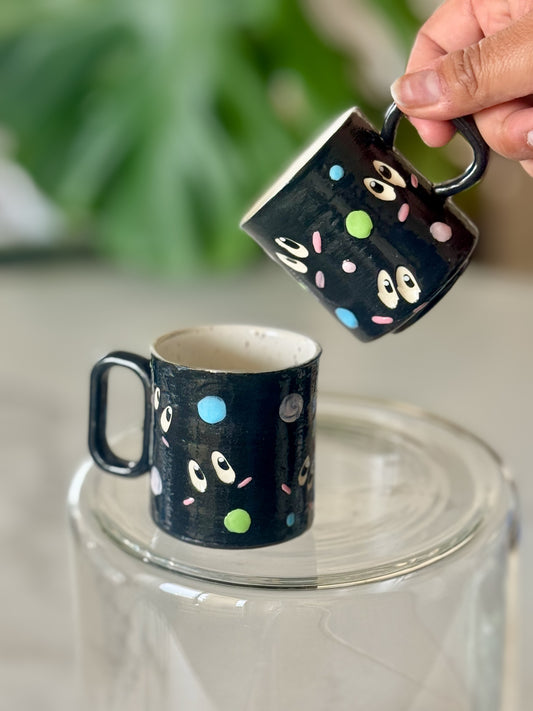 Soot sprite espresso mug front view showing googly eyes and colorful dots on black glaze