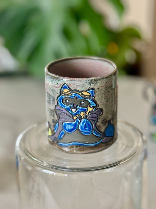 D&D raccoon adventurer handleless cup showing full color raised illustration on speckled grey-green glaze with pink interior