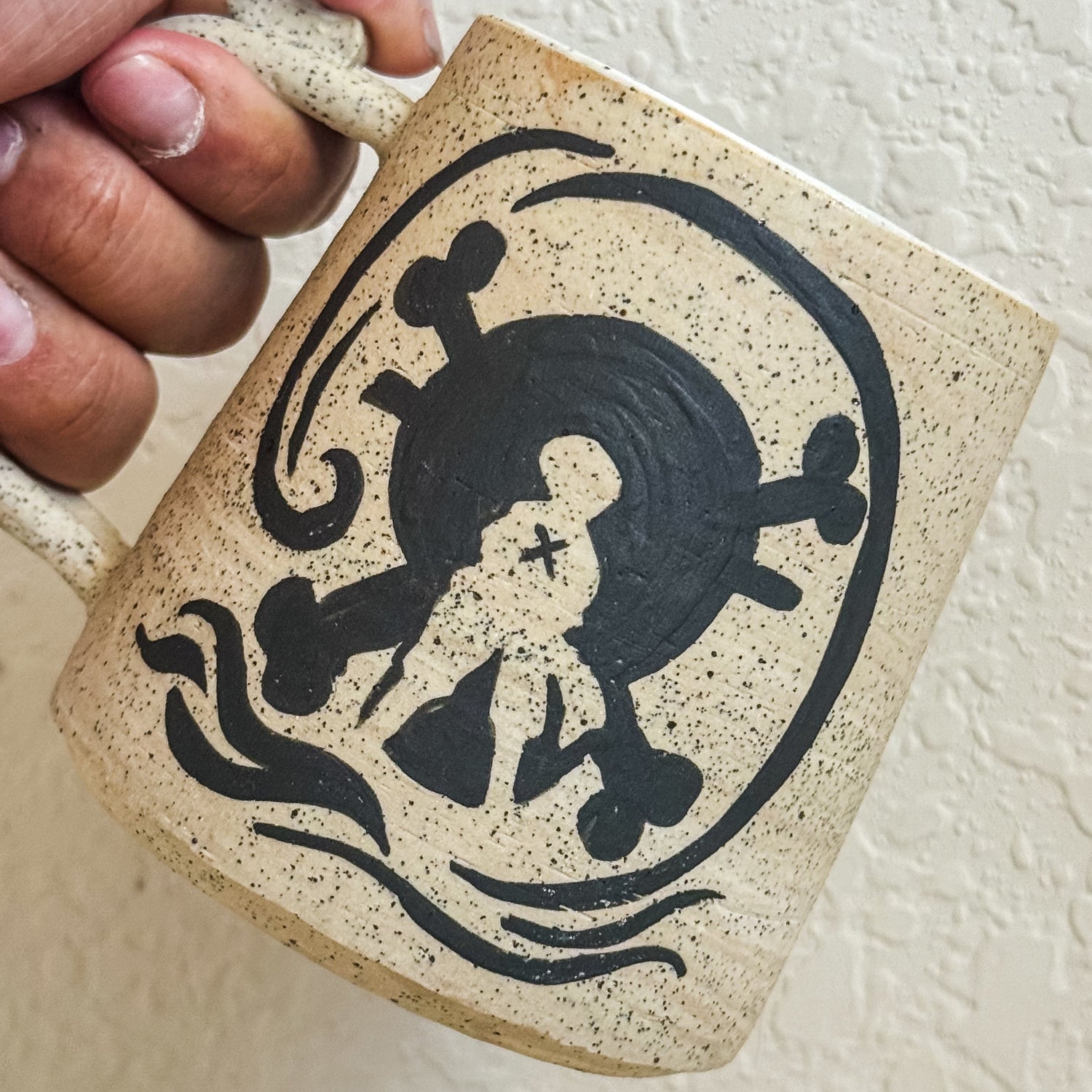Hand holding a ceramic mug with a black silhouette design on a white background